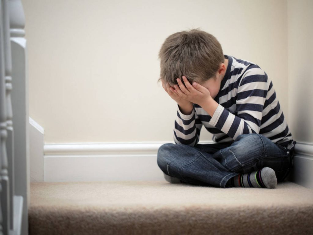 Upset problem child with head in hands sitting on staircase concept for bullying, depression stress or frustration